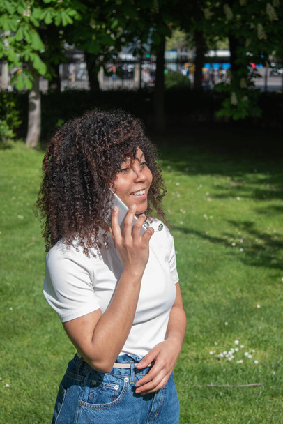Frau mit lockigem Haar telefoniert in einem Naturgebiet - Foto, Bild