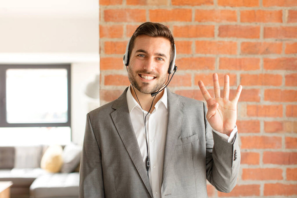 handsome telemarketer smiling and looking friendly, showing number four or fourth with hand forward, counting down - Фото, зображення