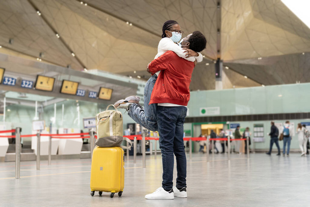 Pár afrických amerických turistů v maskách objetí na letišti, vzrušené setkání milenců po covid-19 - Fotografie, Obrázek