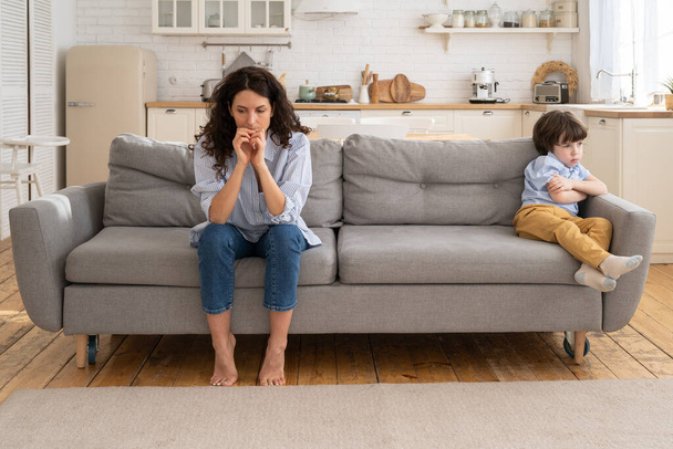 Sértett anya és fia ülnek a kanapén a nappaliban elkerülve a beszélgetést nézik egymást veszekedés után - Fotó, kép