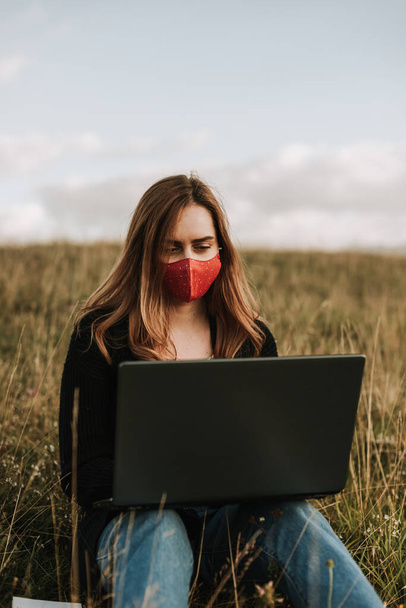 Maskeli kadın dizüstü bilgisayarda çalışıyor, doğada uzak bir yerde. - Fotoğraf, Görsel