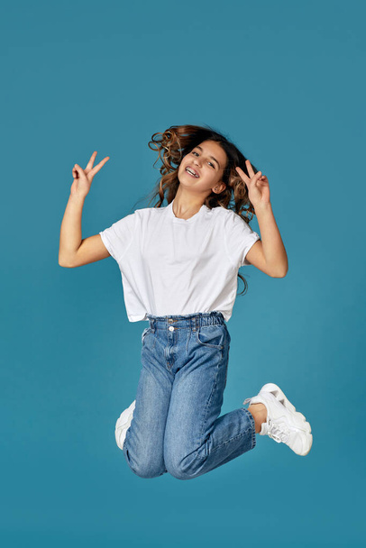curly teen girl in white t-shirt and denim jumping - Фото, изображение