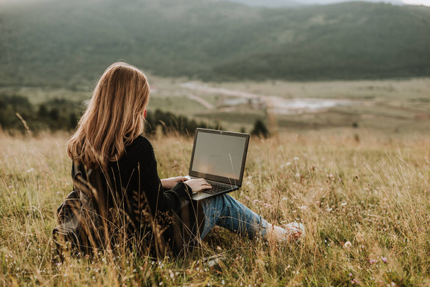 Femme avec masque travaillant sur ordinateur portable, emplacement éloigné dans la nature - Photo, image