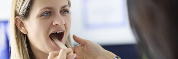Medico guardando la gola della paziente donna con spatola di legno in clinica - Foto, immagini