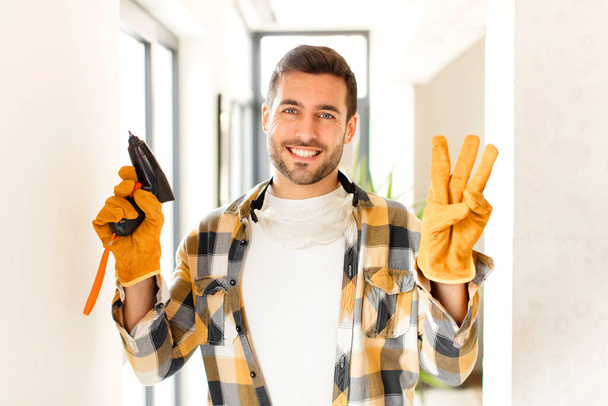handyman smiling and looking friendly, showing number three or third with hand forward, counting down - Фото, изображение
