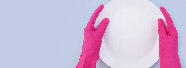 Hands in protective gloves holding white plate on blue background, top view, copy space - Фото, изображение
