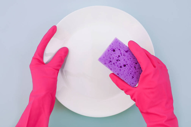 Hands in pink protective gloves washing a plate - 写真・画像