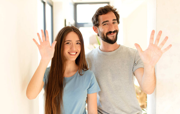 young couple smiling and looking friendly, showing number five or fifth with hand forward, counting down - Photo, image