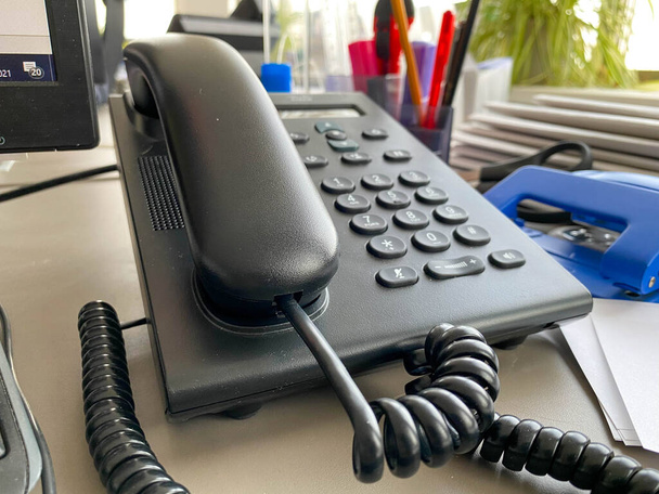Schwarzes Festnetztelefon mit Röhre, Knöpfen und Draht auf dem Arbeitstisch am Bürotisch mit Büromaterial. Geschäftsarbeit. - Foto, Bild