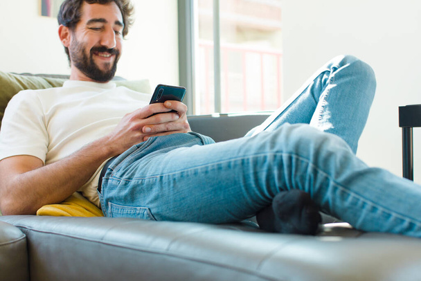 young bearded man resting on a couch with a smart phone - Zdjęcie, obraz