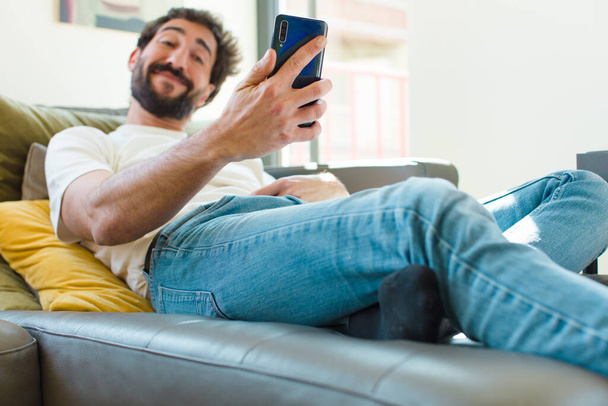 young bearded man resting on a couch with a smart phone - Foto, Imagen