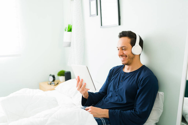 Счастливый человек смотрит комедийный фильм или видео на планшете и смеется, отдыхая на удобной кровати перед сном - Фото, изображение