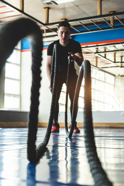 Crossfit with ropes. The athlete is training in the gym opposite large panoramic windows. - Foto, afbeelding