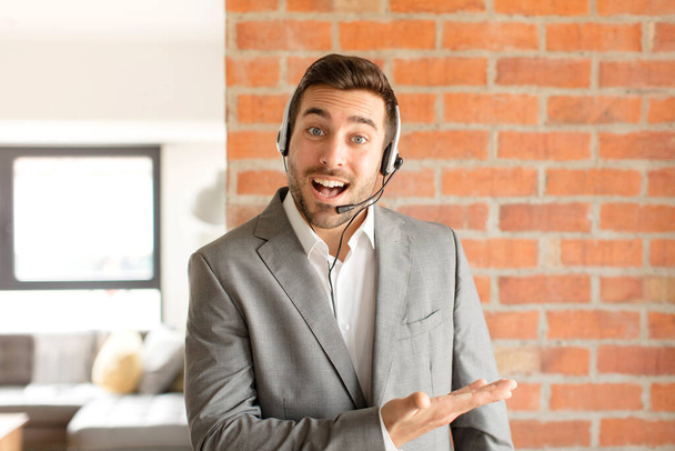 handsome telemarketer smiling cheerfully, feeling happy and showing a concept in copy space with palm of hand - Φωτογραφία, εικόνα