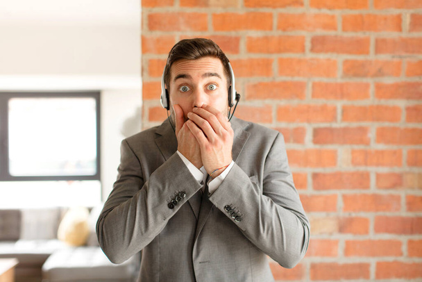 handsome telemarketer covering mouth with hands with a shocked, surprised expression, keeping a secret or saying oops - Foto, Imagen