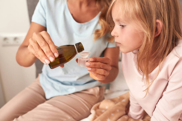Mother gives cough syrup to her ill daughter making a right treatment - Valokuva, kuva