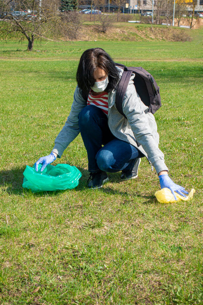Nainen siivoamassa roskia. Vapaaehtoiset kädet sinisillä hanskoilla keräävät roskia muovipussiin. Vapaaehtoistyö, saastuminen, ekologia ja muovi - Valokuva, kuva