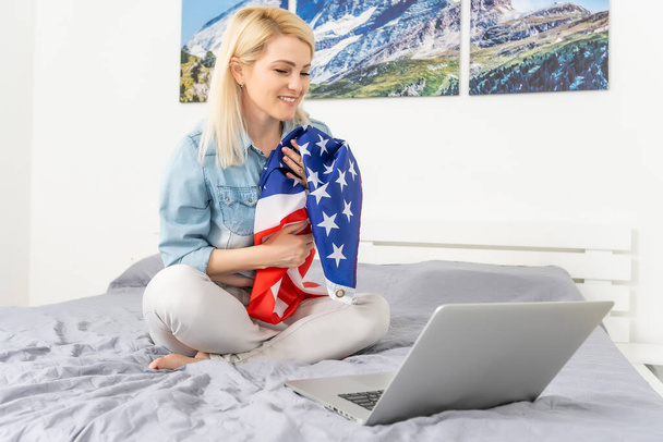 Young woman with USA flag using a laptop computer, independence day online - Photo, Image