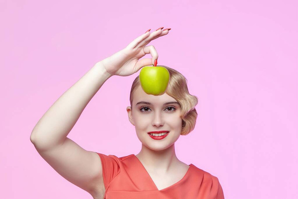 attractive young blonde with a retro hairstyle holds a green apple near her face - Photo, image