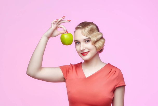 attractive young blonde with a retro hairstyle holds a green apple in her hand - Photo, image