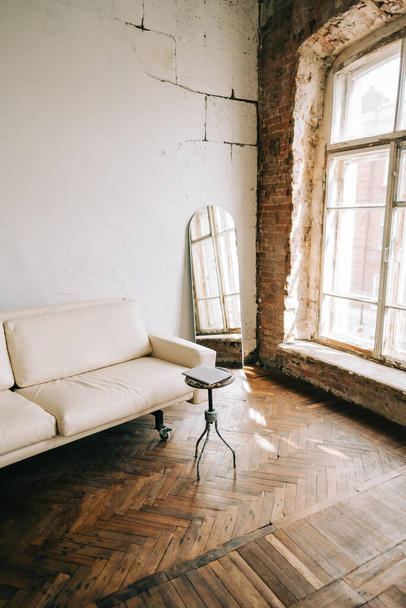 Old fashioned interior big wooden window and mirror, white sofa in old vintage living room with brick walls. - 写真・画像
