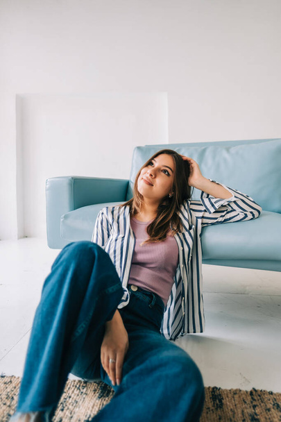 Young calm caucasian woman relaxing, sitting on the floor near sofa in modern living room, lazy happy woman resting at home - Fotoğraf, Görsel
