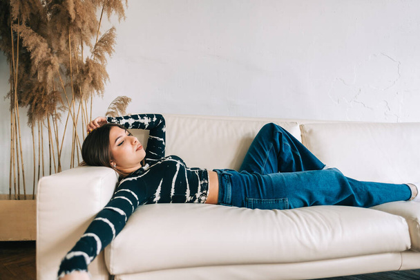 Young calm caucasian woman relaxing lying on comfortable sofa in modern living room, lazy happy woman resting on couch at home - Fotografie, Obrázek
