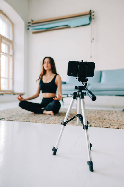 Beautiful brunette fitness woman meditate in front camera on tripod, doing yoga at home. Staying fit and health - Foto, immagini