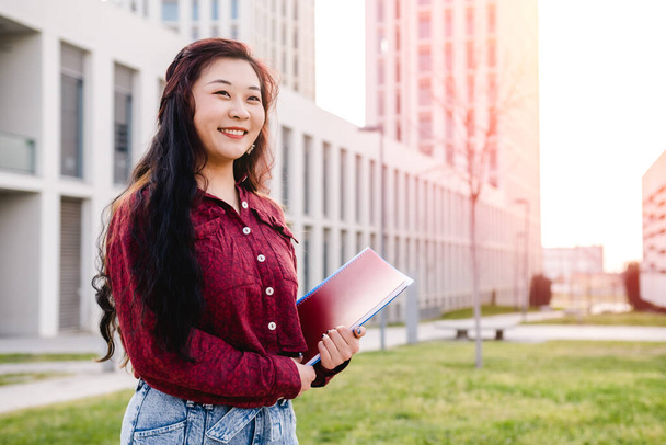 Estudiante asiático sonriendo mientras está de pie al aire libre en el campus universitario. Concepto educativo. - Foto, imagen