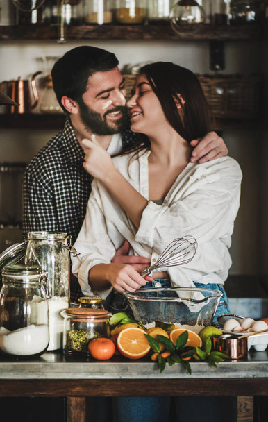 Sweet young family couple cooking together in kitchen. Young caucasian man and brunette woman with faces stained in flour hugging, laughing and making dough for baking citrus cake. Valentines Day - Fotoğraf, Görsel