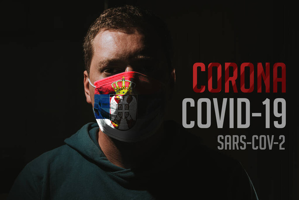 человек в маске с флагом Сербии для защиты от коронного вируса covid-19 SARS-CoV-2 - Фото, изображение