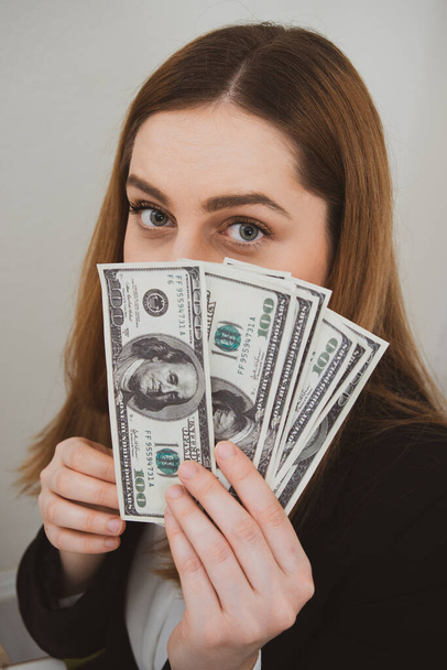 Worried and stressed young woman holding money dollars in hand in office on white background - Foto, afbeelding