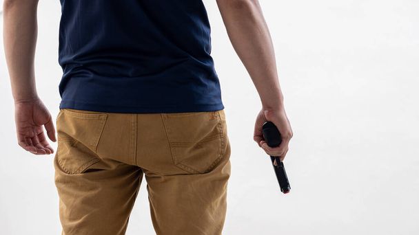 Un hombre con jeans amarillos sostiene un arma en el fondo blanco - Foto, Imagen