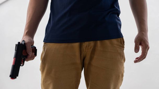 Мужчина в жёлтых джинсах держит пистолет на белом фоне - Фото, изображение