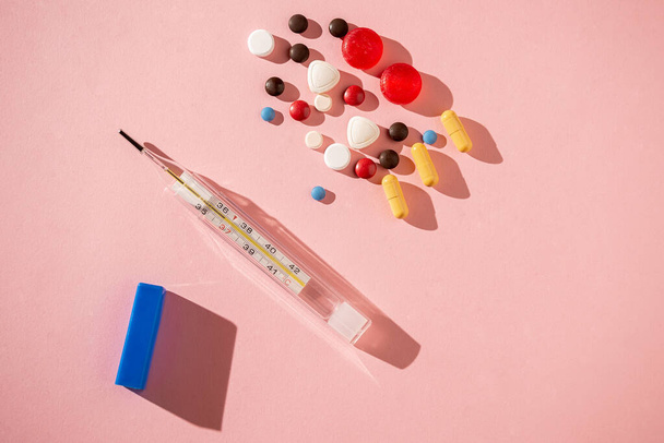 Termômetro médico e pílulas coloridas em fundo rosa - Foto, Imagem