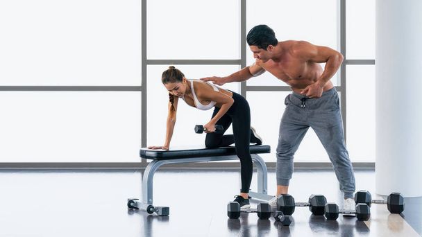 caucasian male gym trainer coaching and help asian athletic woman workout with dumbbell weight lifting for bodybuilding in gym and fitness club - Photo, image