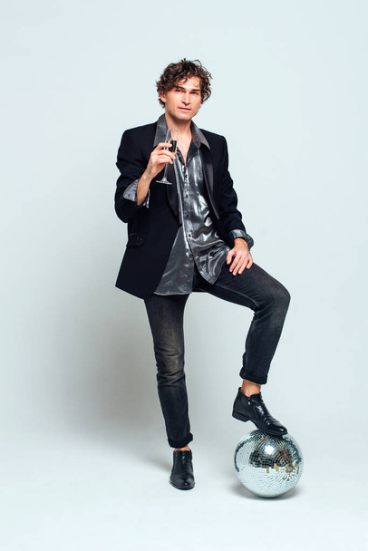 Tall handsome confident young man in a jacket holding glass of wine over white background - 写真・画像
