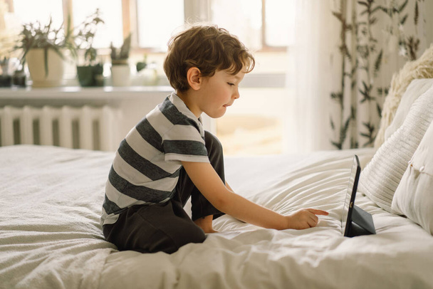 Little Boy met een tablet in de kamer. De jongen speelt spel op de tablet. Technologie concept. Kind met een gadget - Foto, afbeelding