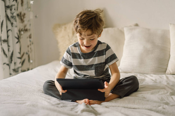Niño pequeño con una tableta en la habitación. El chico juega en la tableta. Concepto tecnológico. Niño con un gadget - Foto, Imagen