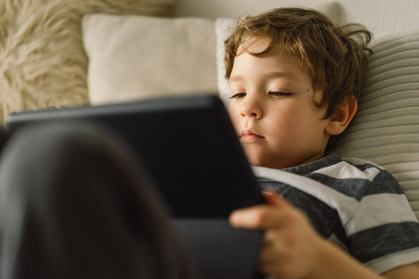 Kleiner Junge mit einem Tablet im Zimmer. Der Junge spielt ein Spiel auf dem Tablet. Technologiekonzept. Kind mit Spielzeug - Foto, Bild