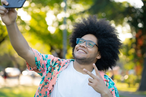 Latin man taking a selfie with phone outdoors. - Fotografie, Obrázek
