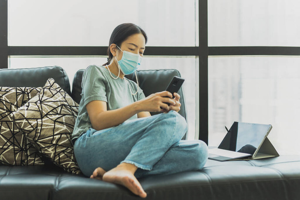 Woman wearing protective mask sit on couch using smartphone in quarantine. - Foto, Bild