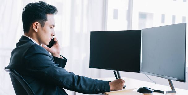 アジアのビジネスの人々は電話での作業に焦点を当てています。2つの空白の画面を持つコンピュータ - 写真・画像