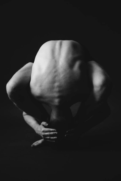 Yoga workout.  Man performs yoga asanas on dark background. Stylish studio sports photography - Photo, Image