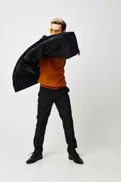 nice guy in trousers and an orange sweater Dark coat model light background - Photo, Image