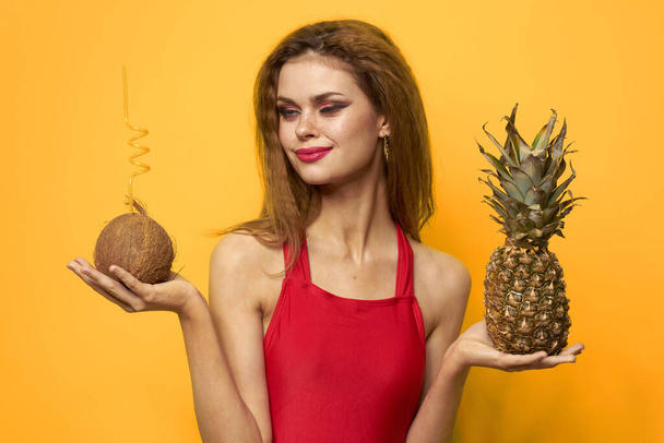 woman with coconut cocktail Pineapple in hands and critical fruits Red t-shirt yellow background - Photo, Image