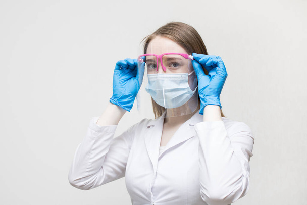 The blonde doctor confidently and professionally wears a medical mask and a protective screen. Female doctor in a medical mask and gloves. Doctor or scientist concept. - Foto, Imagen