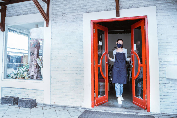florist woman wearing apron and face mask standing open the door flower shop - Foto, imagen