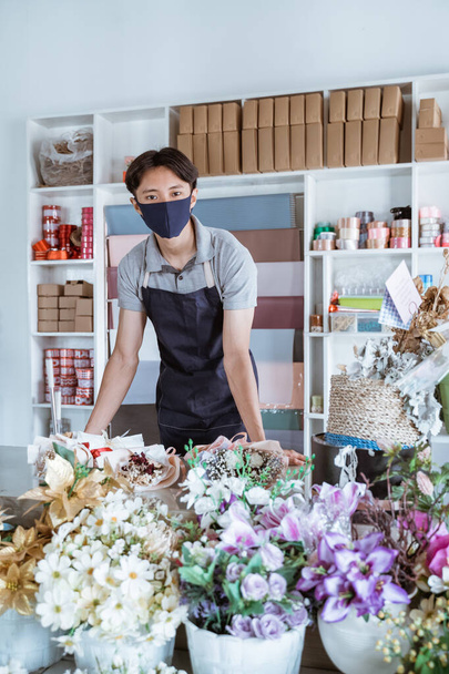 florist man wearing face mask standing behind a flower bouquet - Фото, зображення