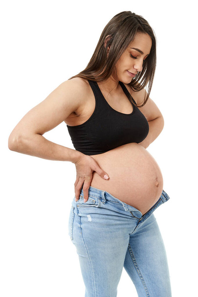 Pregnant woman trying to fit in her too tight jeans, isolated on white background - Foto, Imagem